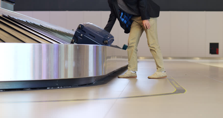 Passenger man walks to baggage carousel, takes his large suitcase, places it on floor, extends telescopic handle and roll it away. Typical scene at luggage claim hall at modern international airport