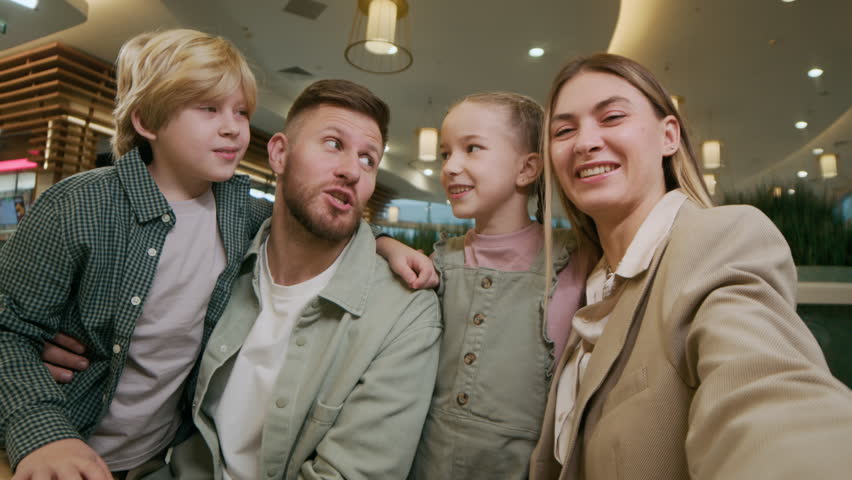 POV shot of Caucasian family of four looking at camera and vlogging while visiting food court in shopping mall at weekend