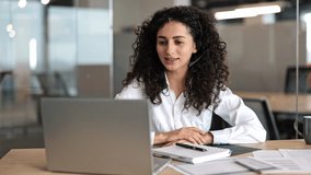 Smiling businesswoman with curly hair and headset talks at laptop during a video conference in modern office. - Powered by Shutterstock - Get 15% off with code: PIKWIZARD15