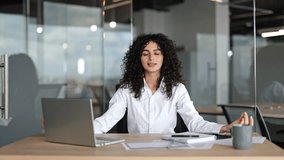 Young businesswoman with curly hair meditates in modern office. Woman takes a break from work to practice mindfulness and stress reduction. - Powered by Shutterstock - Get 15% off with code: PIKWIZARD15