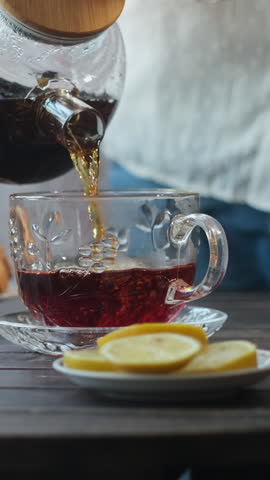 Vertical video. Tea party. Woman serves hot brewed black tea into a cup