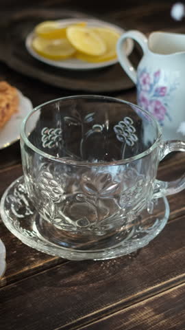 Vertical video. Tea time. Pouring brewed black tea from teapot into transparent cup. Breakfast with tea and pastries. 