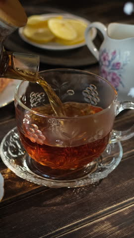 Vertical video. Tea time. Pouring brewed black tea from teapot into transparent cup. Breakfast with tea and pastries. 
