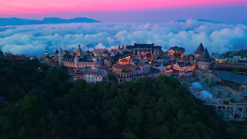Aerial view is lunar castles of Bana Hills at pink sunset time with clouds down. The famous tourist destination of Da Nang, Vietnam. Near Golden bridge.