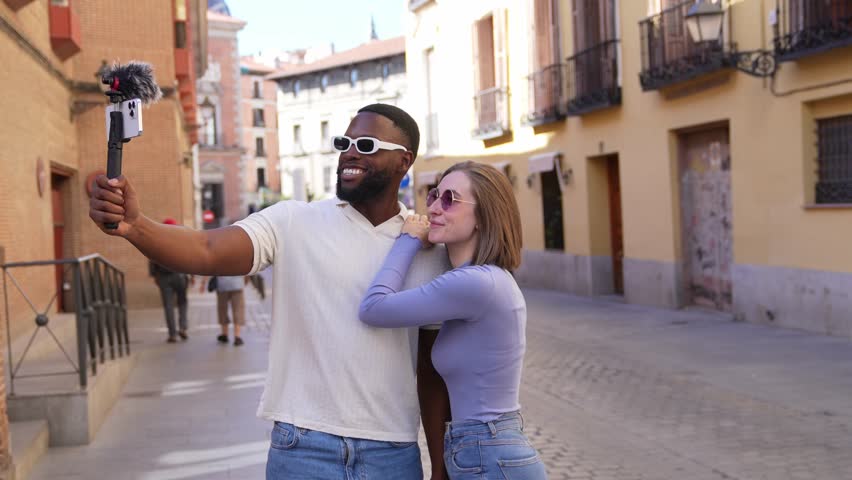 Multiracial couple recording travel video blog, capturing vibrant moments while exploring picturesque european urban landscape with spontaneous energy