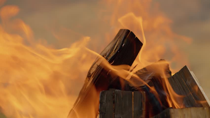 Crackling wood fire burning intensely, casting orange and yellow flames while preparing outdoor barbecue grill with intense heat and energy