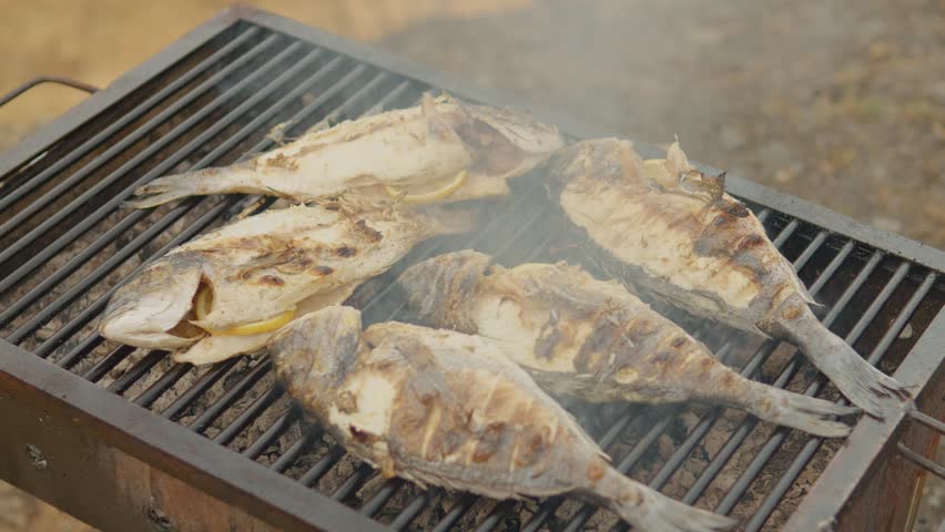 Delicious sea bream fish grilling on a barbecue, seasoned with lemon slices, emitting smoke and aroma