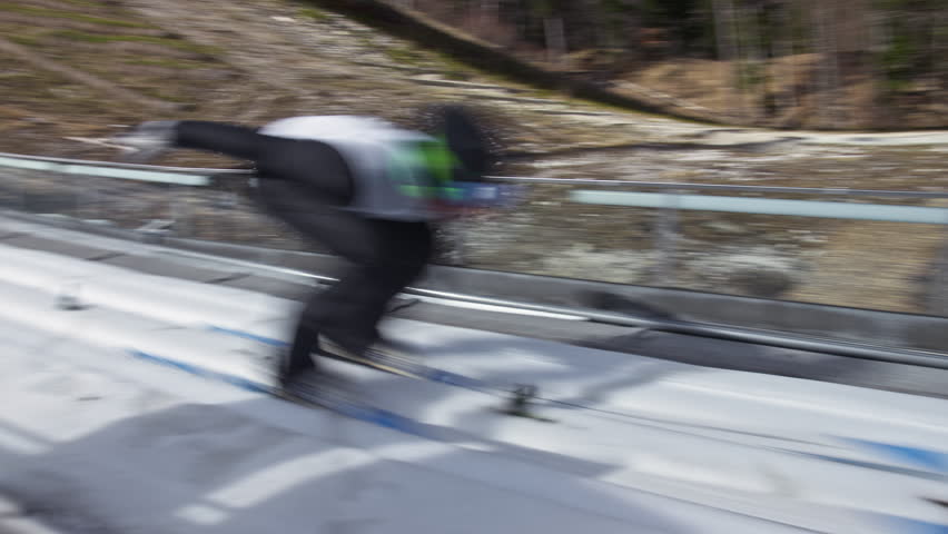 Ski jumper running down the ski jumping hill, flying and landing on a landing slope, handheld shot. Winter sports venue concept.