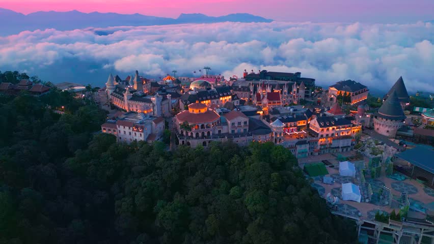Aerial view is lunar castles of Bana Hills at pink sunset time with clouds down. The famous tourist destination of Da Nang, Vietnam. Near Golden bridge.