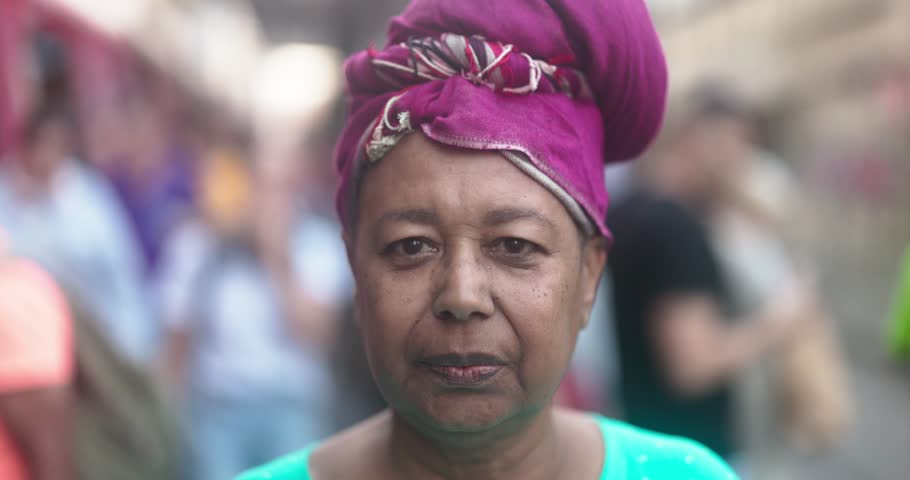 African senior woman wearing traditional dress and looking on camera in the city at tram station - Elderly lifestyle and culture concept 
