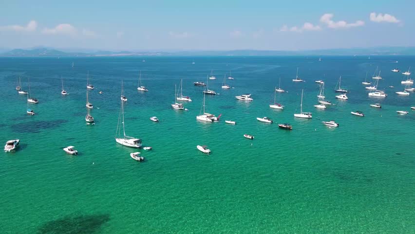 Summer travel destination in south of France, Porquerolles Island. Dozens of boats and yachts in the bay. Aerial drone perspective. Calm water. Turquoises water colour.