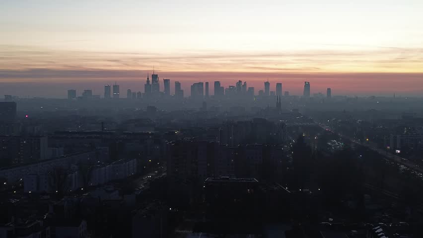A cinematic drone shot of Warsaw at dusk, where the red sunset paints the sky above the iconic cityscape and modern high-rises.