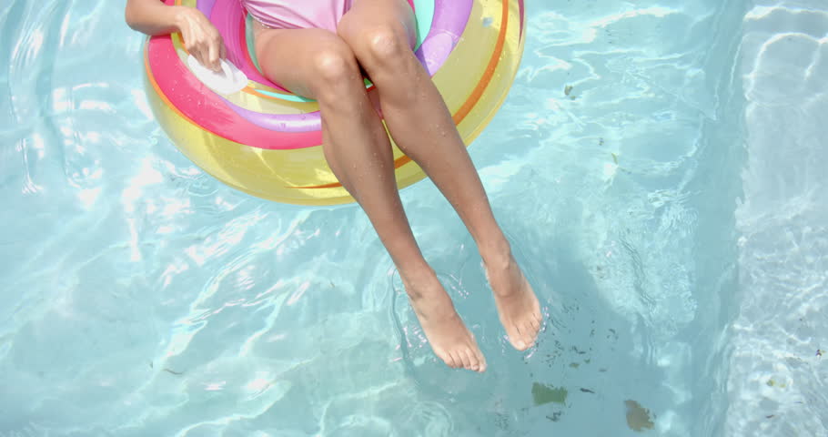 Biracial young woman relaxing in pool on inflatable ring at home, copy space. Wearing pink nail polish, enjoying water with light brown skin, unaltered, slow motion