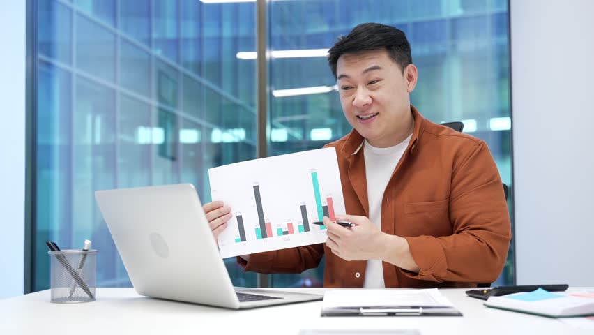 Professional asian male manager presenting chart data at workspace in the office. Businessman discussing growth statistics by video call using laptop. Business meeting, analysis, and teamwork concepts - Powered by Shutterstock - Get 15% off with code: PIKWIZARD15