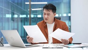 Confused asian businessman having difficulty with paperwork sitting at a desk at workplace in business office. Puzzled male worker checking documents on computer and cannot understand problem - Powered by Shutterstock - Get 15% off with code: PIKWIZARD15