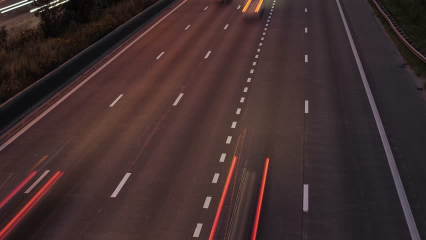 A timelapse view of nighttime highway traffic featuring red tail light motion trails and dynamic speed