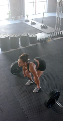 Vertical video: Lifting barbell, woman in gym focusing on strength training workout. Exercise, fitness, weightlifting, bodybuilding, muscles, athlete