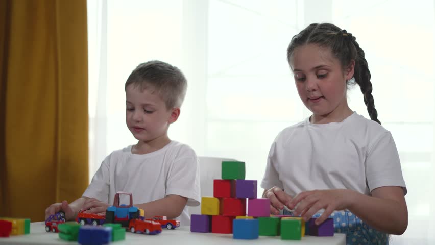 Children play with cubes build tower table. Developing builder skills teamwork and creativity. Children support each other play build colorful tower blocks while learning in fun environment at table.