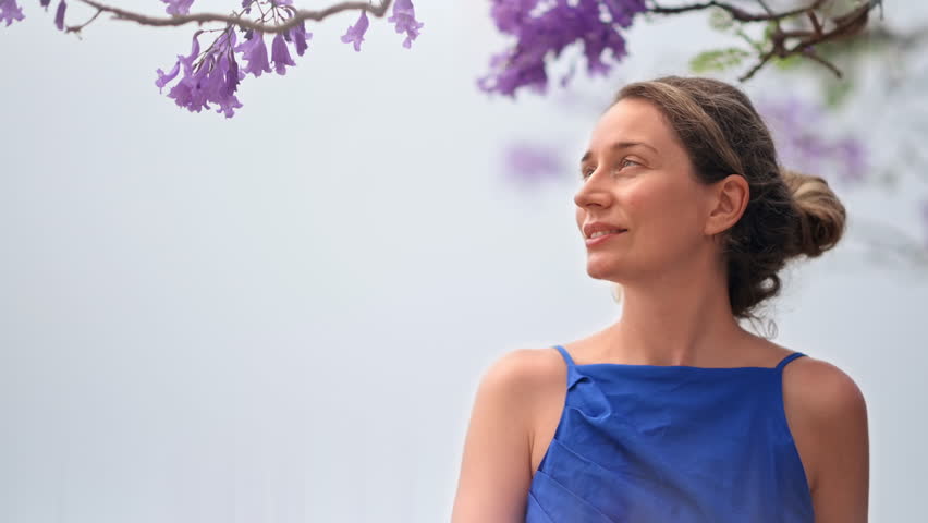 Caucasian woman in blue dress posing, tree with pink flowers in Barcelona, Spain