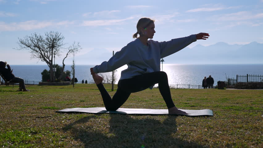 Girl doing yoga in the park with the sea and mountains in the background.