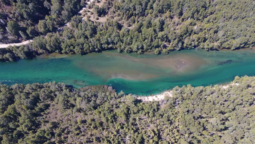Panning aerial movement above the river between a dense green forest, Parque Nacional Los Alerces, Patagonia, Argentina.