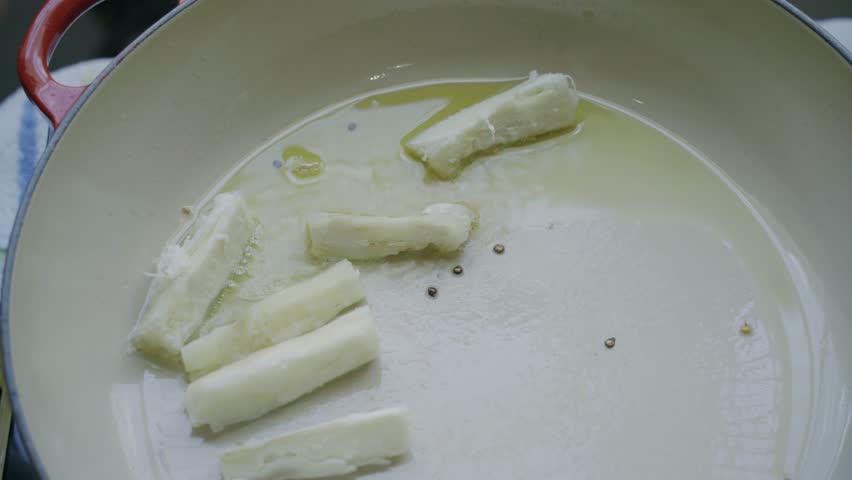 Frying cassava sticks in oil alongside peppercorns in a white pan, creating a vibrant scene of a chef preparing a traditional South American dish bursting with flavor