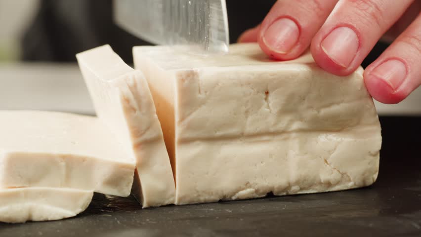 Fried tofu with sesame seeds and spices on cast iron pan, cooking japanese salad. Healthy ingredient for cooking vegan vegetarian diet food. Roasted tofu over black background.