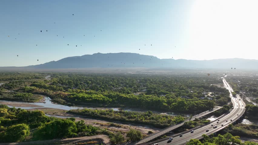 Drone POV of multiple hot air balloons flying over Albuquerque, New Mexico in early morning near the Sandia Mountains.
