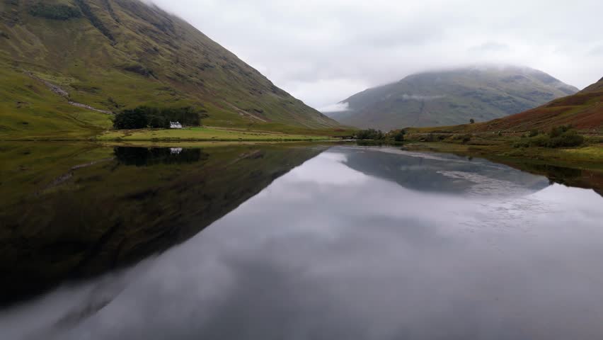 Aerial drone footage of the Glencoe mountain range in the Scottish Highlands, taken in summer on a clear but misty day, morning time.