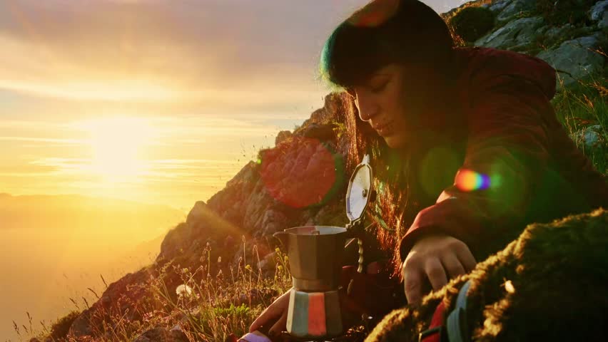 Young woman preparing coffee at sunset during a bivouac in the mountains with his dog