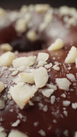 Chocolate donut with nuts rotating. Unhealthy food. Glazed donut with sprinkles. Bakery and food concept. Delicious donut. Vertical video. Close-up in 4K, UHD