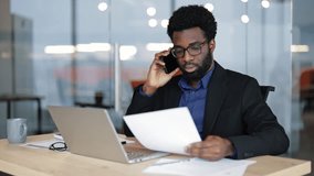 Serious businessman talking on the phone and looking at documents while sitting at his desk. He is working inside a bright office during the daytime. - Powered by Shutterstock - Get 15% off with code: PIKWIZARD15