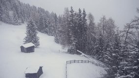 Two small rustic cabins are nestled on a snowy hillside, framed by dense pine trees and a wooden fence. Aerial view, parallax shot. - Powered by Shutterstock - Get 15% off with code: PIKWIZARD15