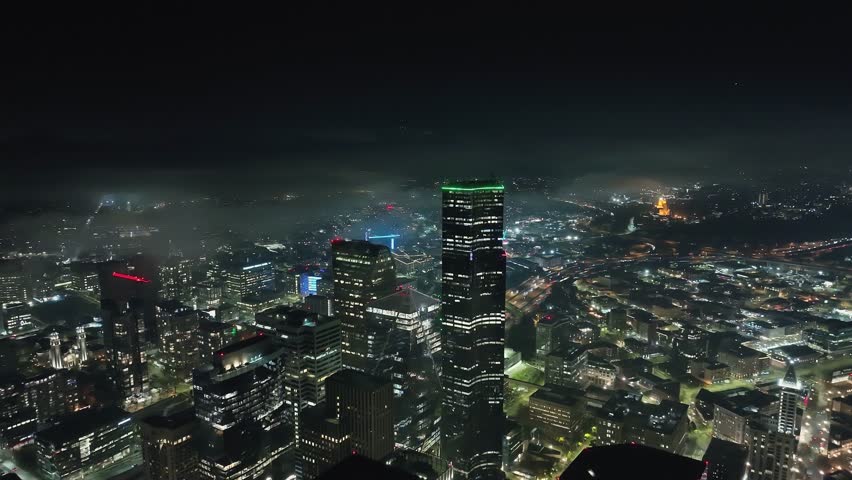 Columbia Center towers above a bright Seattle night cityscape with low clouds