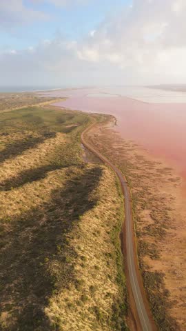Aerial view of a beautiful pink lake with a winding road and rugged coastline, Western Australia, Australia.