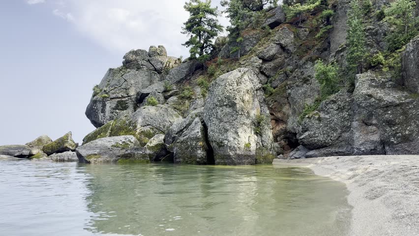 breathtaking view of a rugged coastline with towering rocks lining the shore. The scene is tranquil and serene, with the calm, peaceful waters of a lake gently lapping against the rocky edge