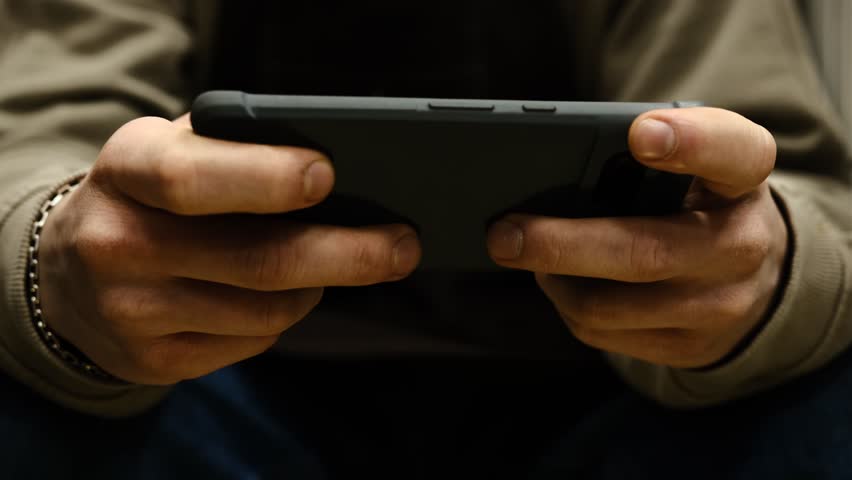 Young man playing mobile game with fast finger movements and colorful pulsating hand lights, dynamic gameplay, close up phone screen, digital entertainment, gaming action, energetic gaming session.