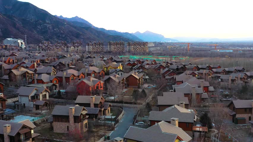 Aerial view of Jackson Hole, a Chinese Copy town near Beijing, China. Bathed in warm sunset hues. Features charming homes, vast landscapes, and distant mountains.