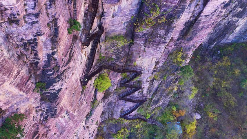 Aerial view of a zigzagging stairway carved into towering cliffs near Xiuyan Village, Zhejiang Province, China, showcasing a perfect harmony of natural beauty and human craftsmanship.