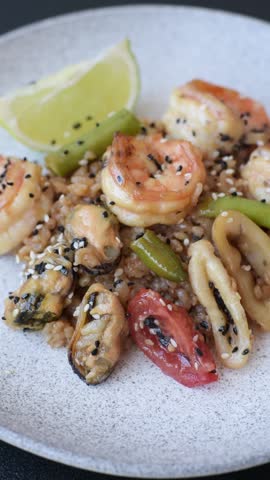 Rice with shrimps and seafood, vegetables, spices and soy sauce on dark concrete background
