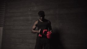 african american athletic man putting on red boxing gloves in a dark room, strong boxer preparing for training and fight - Powered by Shutterstock - Get 15% off with code: PIKWIZARD15