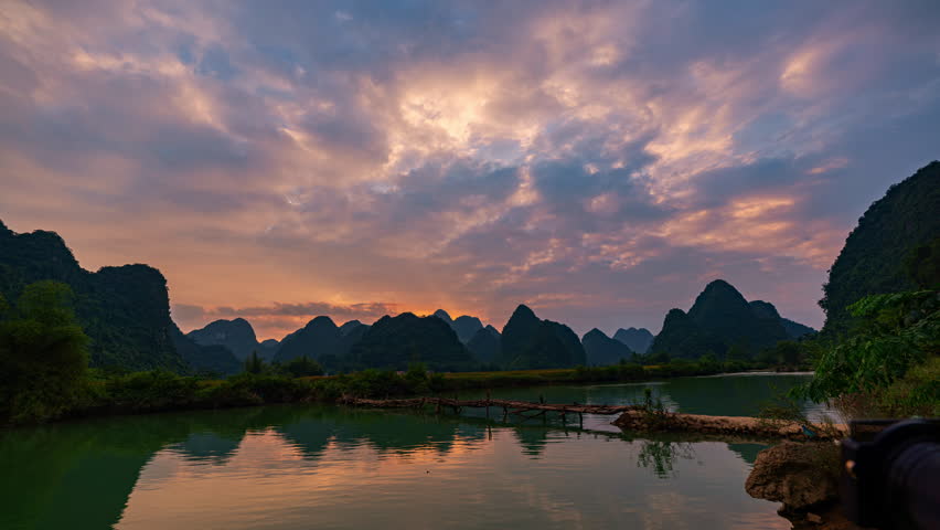 Time lapse amazing Clouds floating in the sky above the mountains in a beautiful twilight. A beautiful reflection of the sky in the canal. There is a wooden bridge to cross the river.beautiful nature