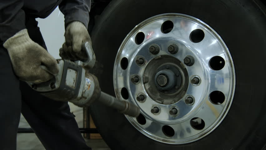 A repair shop worker begins dismantling the wheels on a truck, Various devices and semi truck in a repair shop
