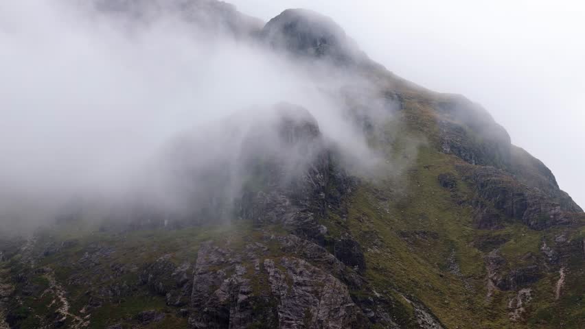 Aerial drone footage of the Glencoe mountain in the Scottish Highlands, taken in summer on a clear but misty day, morning time.