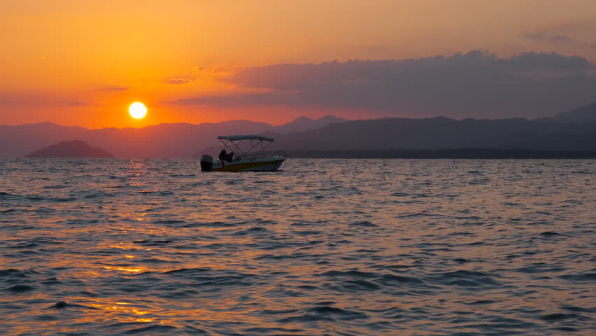 Nightfall horizon with sailing boat. A view of fishing boat slowly floating on sea against colorful horizon in summer.
