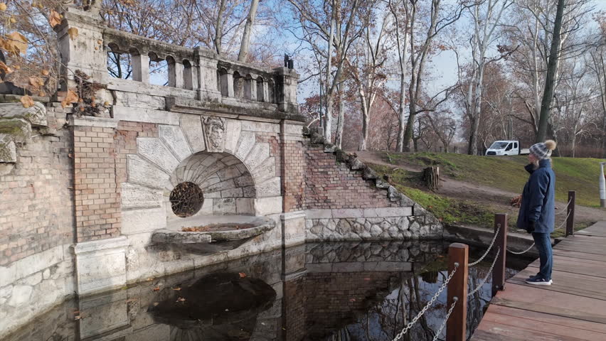 Woman in City Park, Budapest appreciates old fountain and pond, autumn