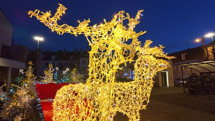 Christmas decorations outdoor, life-size reindeers illuminated at night, red sleigh, French village. Close-up