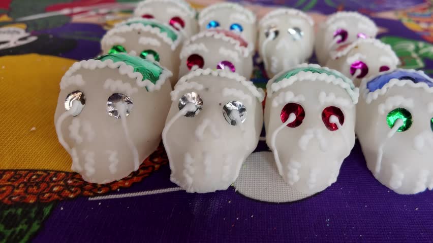 A group of sugar skulls with green and red decorations. The skulls are arranged in a row on a purple tablecloth