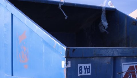 Worker, man dumps a garbage can into a blue dumpster.
