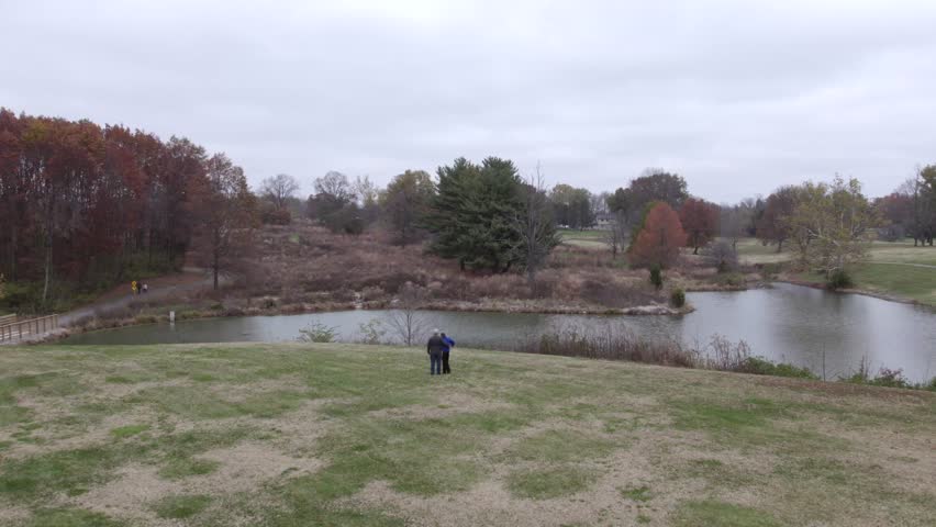 Aerial drone, fly over two people in the park over water in autumn